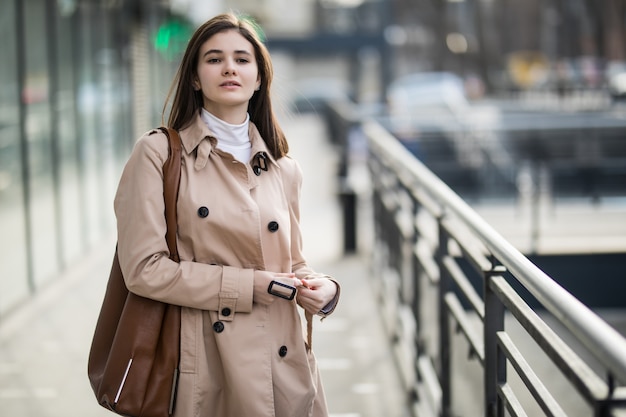 Bella ragazza per strada in cappotto di caffè e borsa in pelle marrone