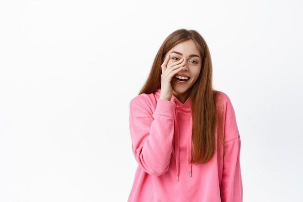 Bella ragazza ridendo e toccando il viso sorridente e guardando felice in piedi su sfondo bianco Copia spazio