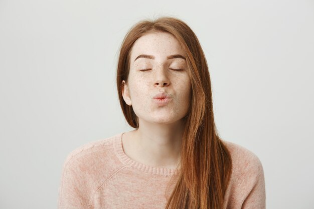 Bella ragazza romantica rossa piega le labbra, soffiando bacio