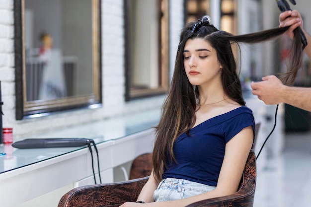 Bella ragazza seduta su una sedia e qualcuno che si fa i capelli dal barbiere Foto di alta qualità