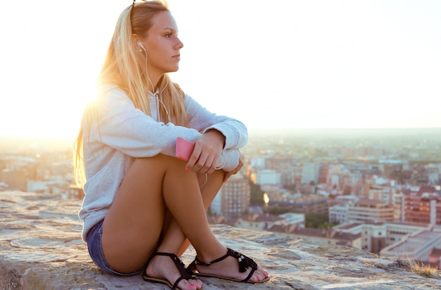 Bella ragazza seduta sul tetto e l&#39;ascolto di musica.