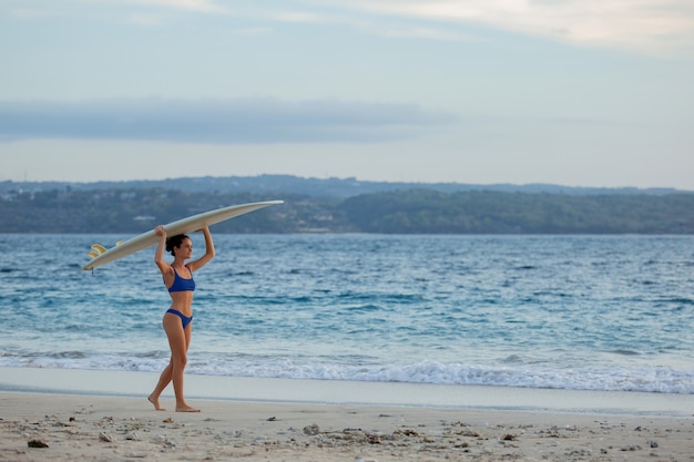 Bella ragazza si trova sulla spiaggia con una tavola da surf.