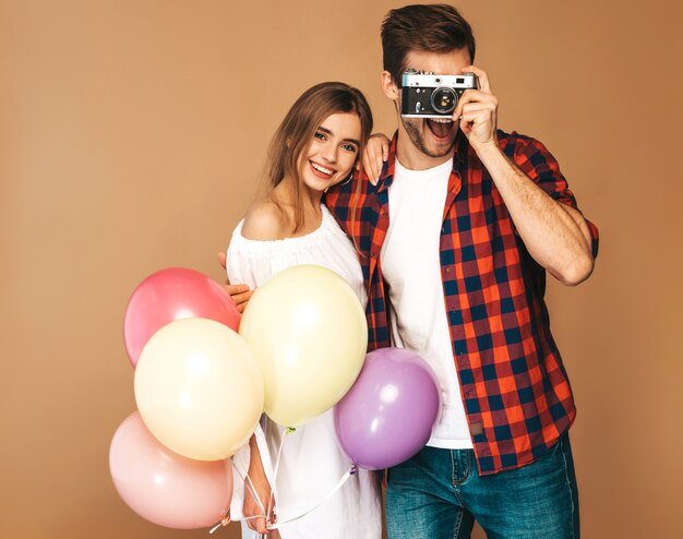 Bella ragazza sorridente e il suo ragazzo bello che tiene mazzo di palloncini colorati. Coppie felici che prendono foto se stessi sulla retro macchina fotografica. Buon compleanno