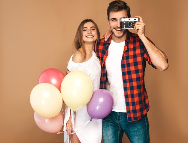 Bella ragazza sorridente e il suo ragazzo bello che tiene mazzo di palloncini colorati. Coppie felici che prendono foto se stessi sulla retro macchina fotografica. Buon compleanno