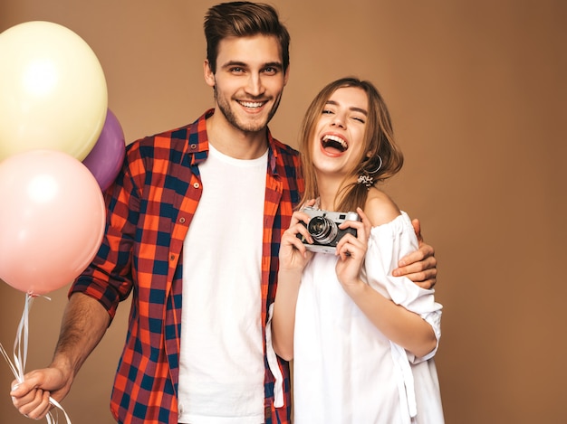 Bella ragazza sorridente e il suo ragazzo bello che tiene mazzo di palloncini colorati. Coppie felici che prendono foto se stessi sulla retro macchina fotografica. Buon compleanno