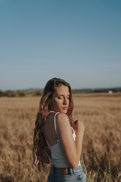 Bella ragazza spagnola bionda che guarda in basso sopra la sua spalla in un soleggiato campo di grano