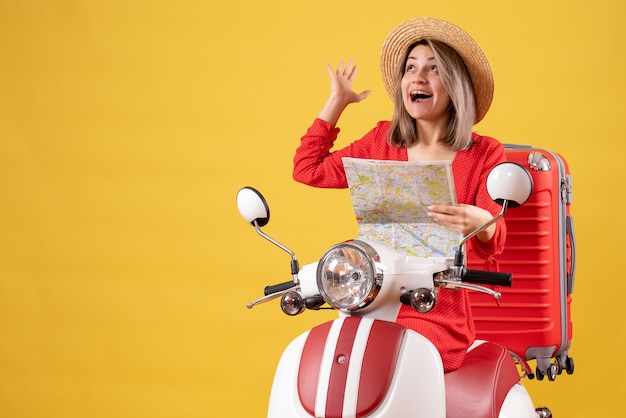 bella ragazza sul motorino con la valigia rossa che tiene la mappa guardando in alto