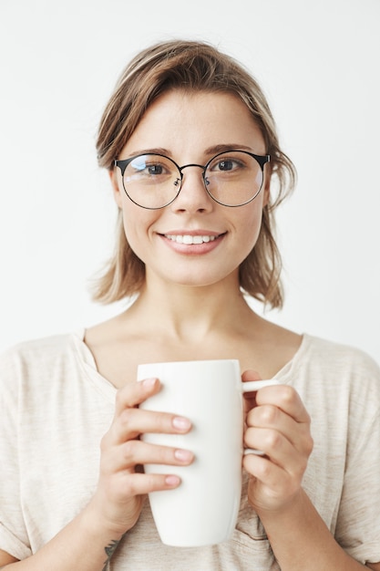 Bella ragazza sveglia in vetri che tengono tazza sorridente.