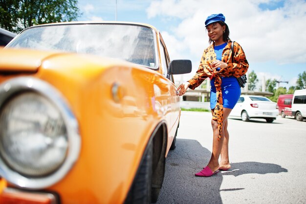 Bella signora afroamericana con occhiali da sole in piedi vicino a un'auto retrò classica arancione