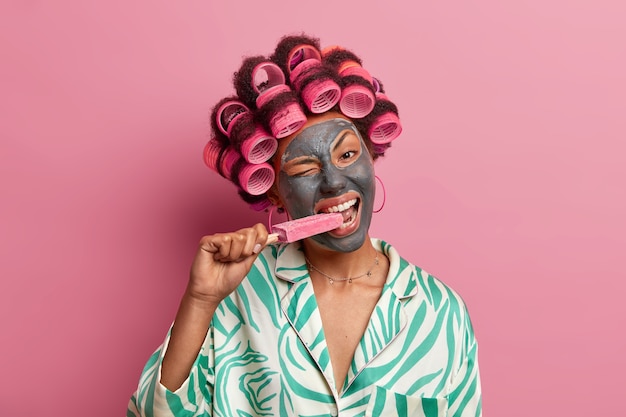 Bella signora che indossa la maschera per la cura del viso indossando bigodini isolati