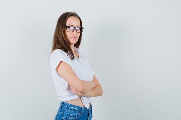 Bella signora che osserva da parte stando in piedi con le braccia incrociate in camicetta bianca, occhiali e guardando fiducioso, vista frontale. spazio per il testo