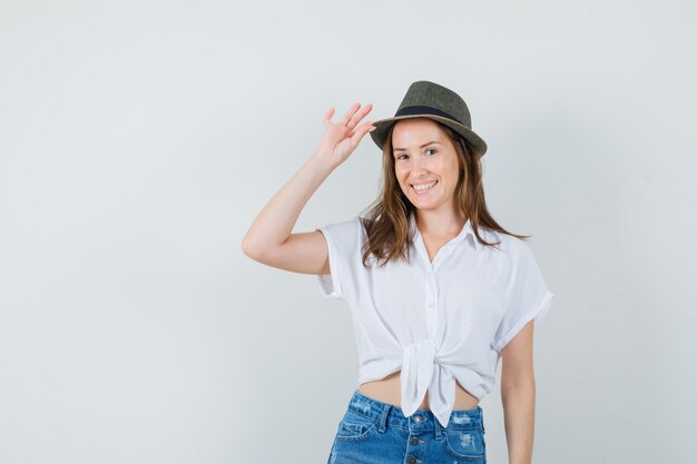 Bella signora che tiene la mano sul cappello in camicetta bianca, cappello e sembra carino.