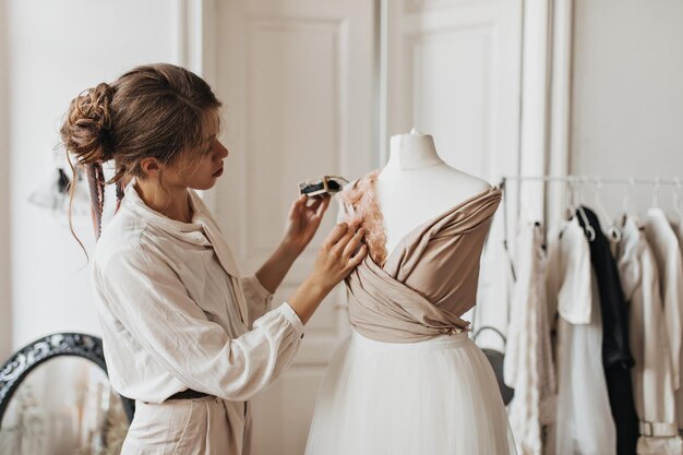 Bella signora in abito beige crea un nuovo vestito Donna bruna in camicia bianca e pantaloni disegnando un vestito alla moda