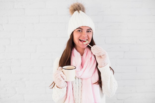 Bella signora in guanti, cappello bobble e sciarpa con tazza e lecca-lecca