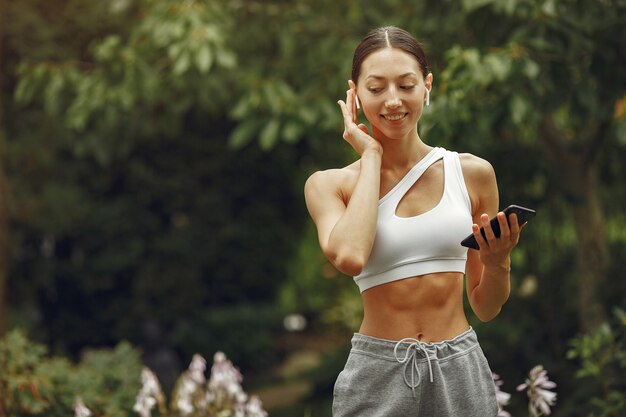 Bella signora in un parco. Bruna con il cellulare. Ragazza in una tuta sportiva.