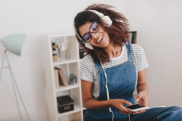 Bella signora nera con gli occhiali rilassante durante l'ascolto della musica preferita con gli occhi chiusi sul posto di lavoro