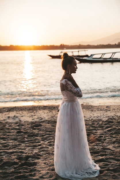 bella sposa in posa sulla spiaggia dietro il mare al tramonto