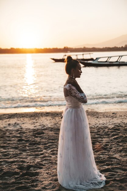 bella sposa in posa sulla spiaggia dietro il mare al tramonto