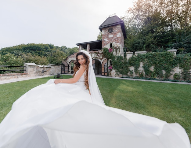 Bella sposa sorridente in abito di lusso sul cortile di erba del vecchio edificio,