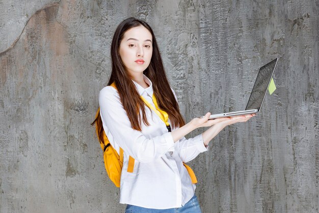Bella studentessa con lo zaino che tiene il computer portatile e lo sguardo. Foto di alta qualità