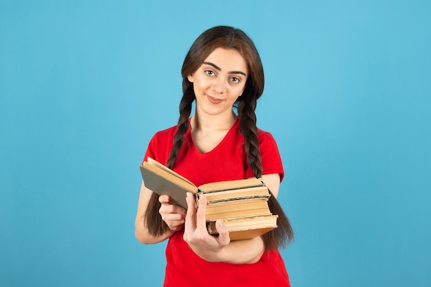 Bella studentessa in maglietta rossa leggendo attentamente il libro sulla parete blu.