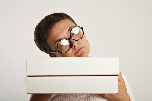 Bella studentessa stanca con gli occhiali rotondi dorme sul suo piano educativo in due pesanti cartelle di documenti