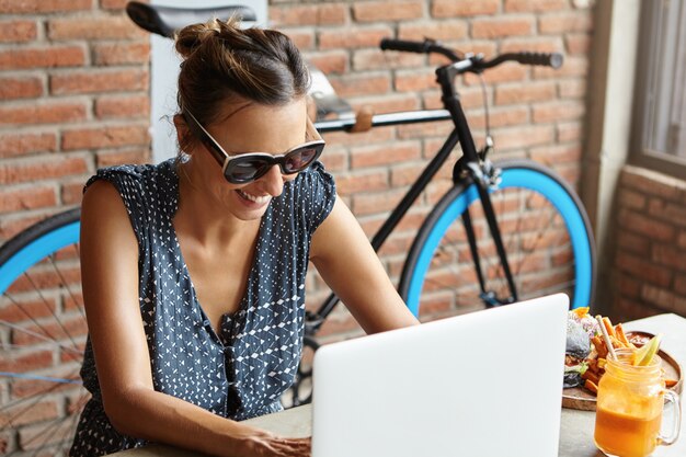 Bella tastiera femminile sul computer portatile generico, godendo della comunicazione online mentre messaggistica amici tramite social media, guardando lo schermo con un sorriso allegro