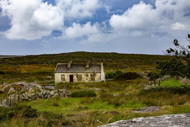 Bella vista di un cottage abbandonato nella contea di Mayo su un campo erboso sotto il cielo nuvoloso