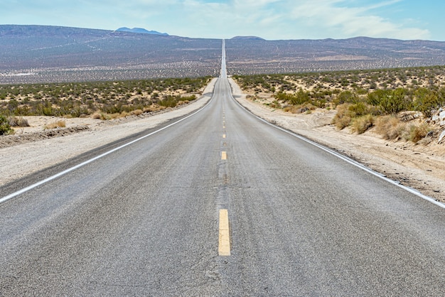 Bella vista di una lunga strada di cemento rettilinea tra il campo del deserto