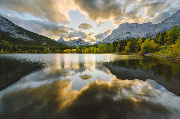 Bella vista di uno stagno che riflette gli alberi verdi sulla riva circondata da montagne innevate