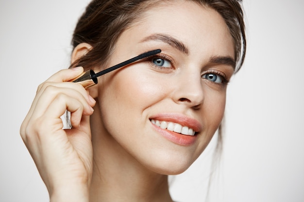 Belle ciglia di tintura sveglie della ragazza che sorridono esaminando macchina fotografica sopra fondo bianco. Concetto di salute e cosmetologia di bellezza.