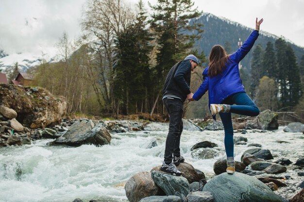 Belle coppie giovani hipster nell'amore che cammina su una roccia al fiume nella foresta di inverno