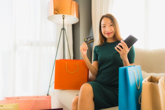 Belle giovani donne asiatiche del ritratto che per mezzo del telefono cellulare con la carta di credito per acquisto online
