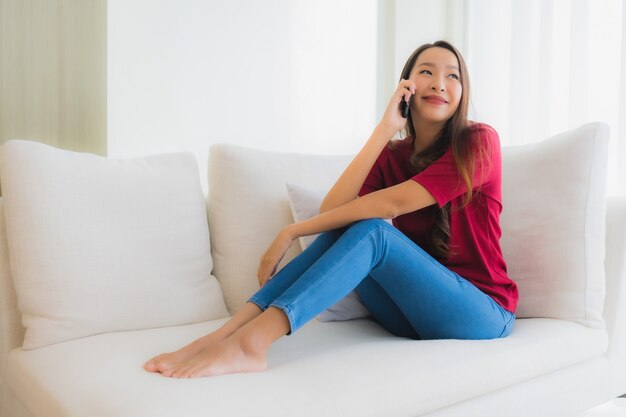 Belle giovani donne asiatiche del ritratto che usando cellulare o Smart Phone sul sofà