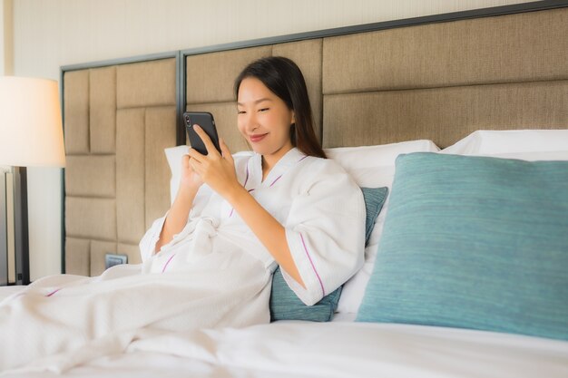 Belle giovani donne asiatiche del ritratto che usando cellulare sul letto