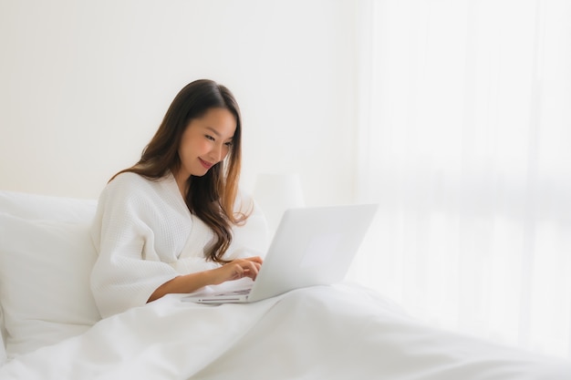 Belle giovani donne asiatiche del ritratto con il computer portatile del computer sul letto