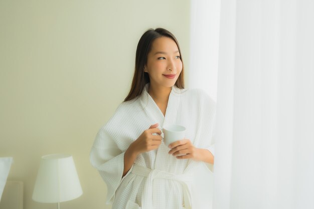 Belle giovani donne asiatiche del ritratto con la tazza di caffè in camera da letto
