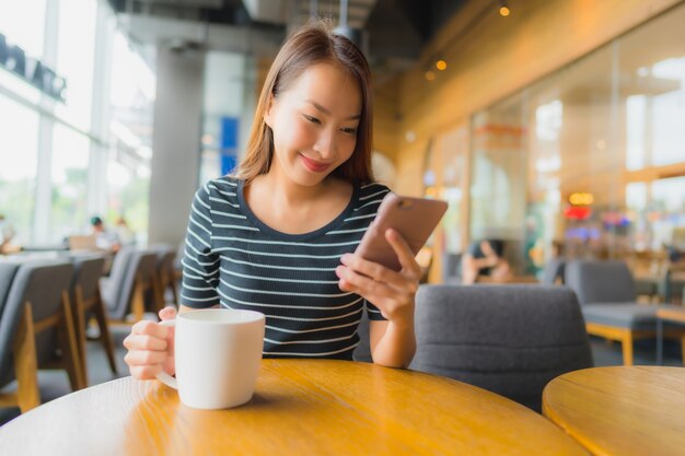 Belle giovani donne asiatiche del ritratto nel caffè e nel ristorante della caffetteria con il telefono cellulare