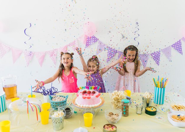 Belle ragazze godendo la festa di compleanno a casa con varietà di cibo e succo sul tavolo