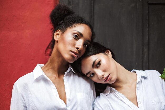 Belle ragazze in camicie bianche che guardano premurosamente da parte le teste appoggiate l'una sull'altra isoalted