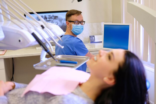 Bellezza bruna femminile in attesa mentre il dentista lavora su un computer. Visita odontoiatrica.