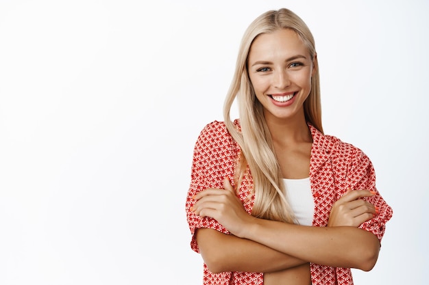 Bellezza e assistenza sanitaria delle donne Giovane donna sorridente felice con i capelli biondi in posa con le braccia incrociate su sfondo bianco