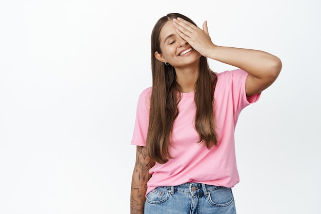 Bellezza. Modello femminile spensierato contro un lato del viso, tocca la pelle del viso con gli occhi chiusi e compiaciuto, sorriso romantico su bianco