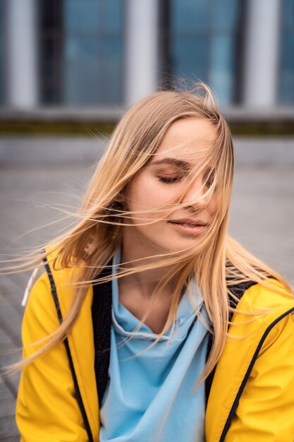 Bellissima giovane donna bionda per strada, in posa con il vento tra i capelli