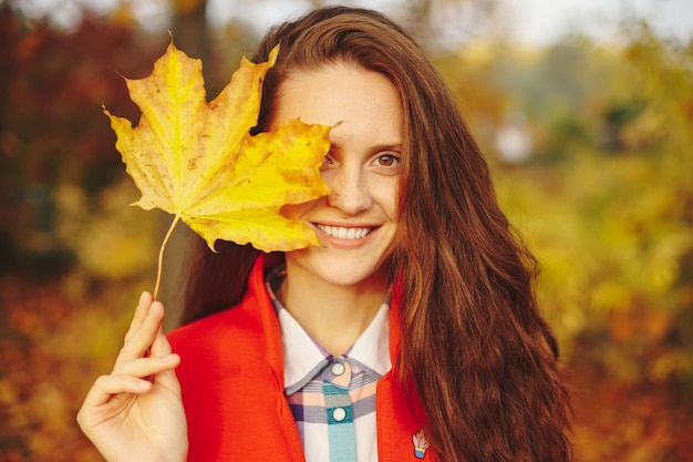 Bellissima giovane donna con lunghi capelli ondulati che copre il viso con una foglia