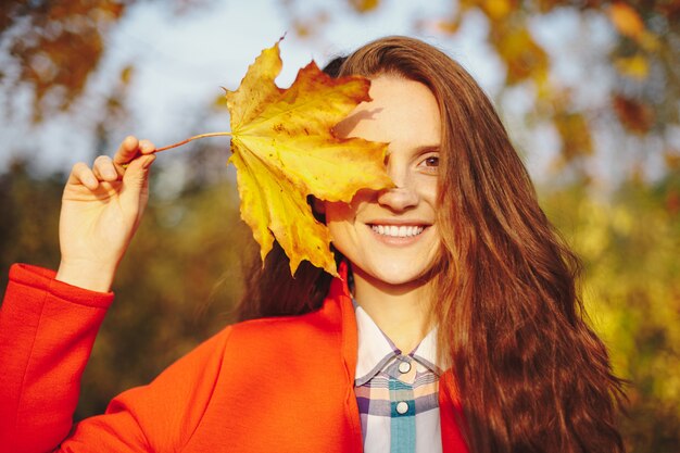 Bellissima giovane donna con lunghi capelli ondulati che copre il viso con una foglia