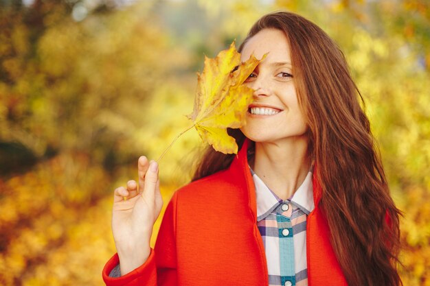 Bellissima giovane donna con lunghi capelli ondulati che copre il viso con una foglia