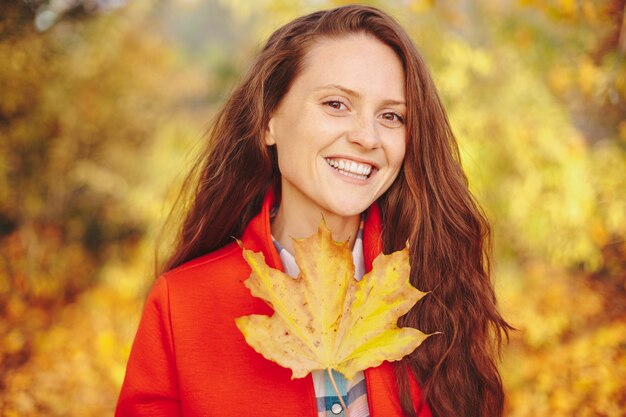 Bellissima giovane donna con lunghi capelli ondulati che copre il viso con una foglia