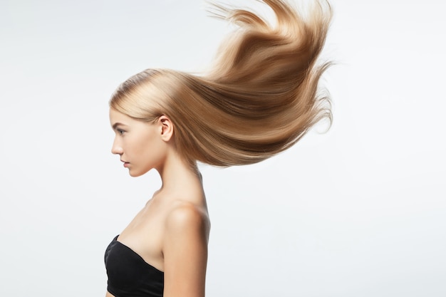 Bellissima modella con lunghi capelli biondi lisci e volanti isolati su sfondo bianco studio. Giovane modello caucasico con pelle ben tenuta e capelli che soffia in aria.