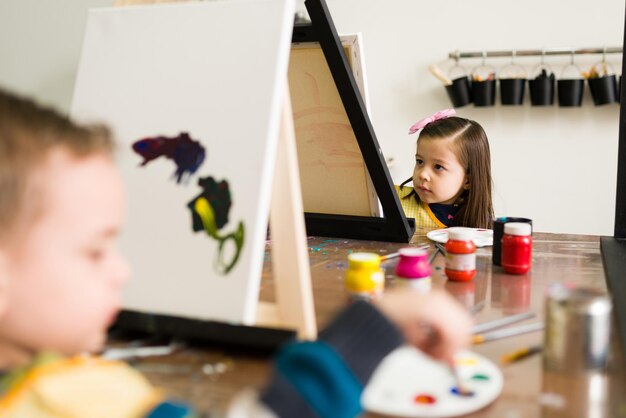 Bellissimi bambini elementari con grembiuli stanno dipingendo su una tela durante una lezione per bambini nella scuola d'arte